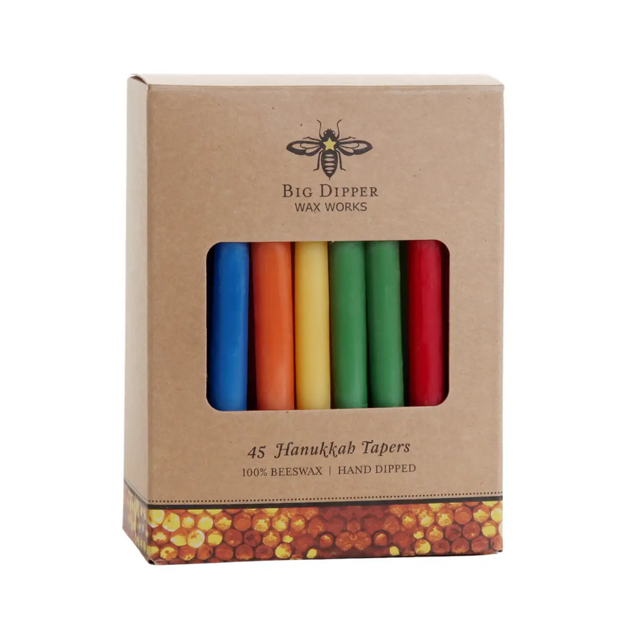 A boxed set of hand-dipped Hanukkah taper candles in blue, orange, yellow, green, white, and red, presented in a brown kraft paper box with a honeycomb pattern at the bottom. The brand 'Big Dipper Wax Works' is clearly printed on the front. Available at Luca Essentials in Los Angeles. 