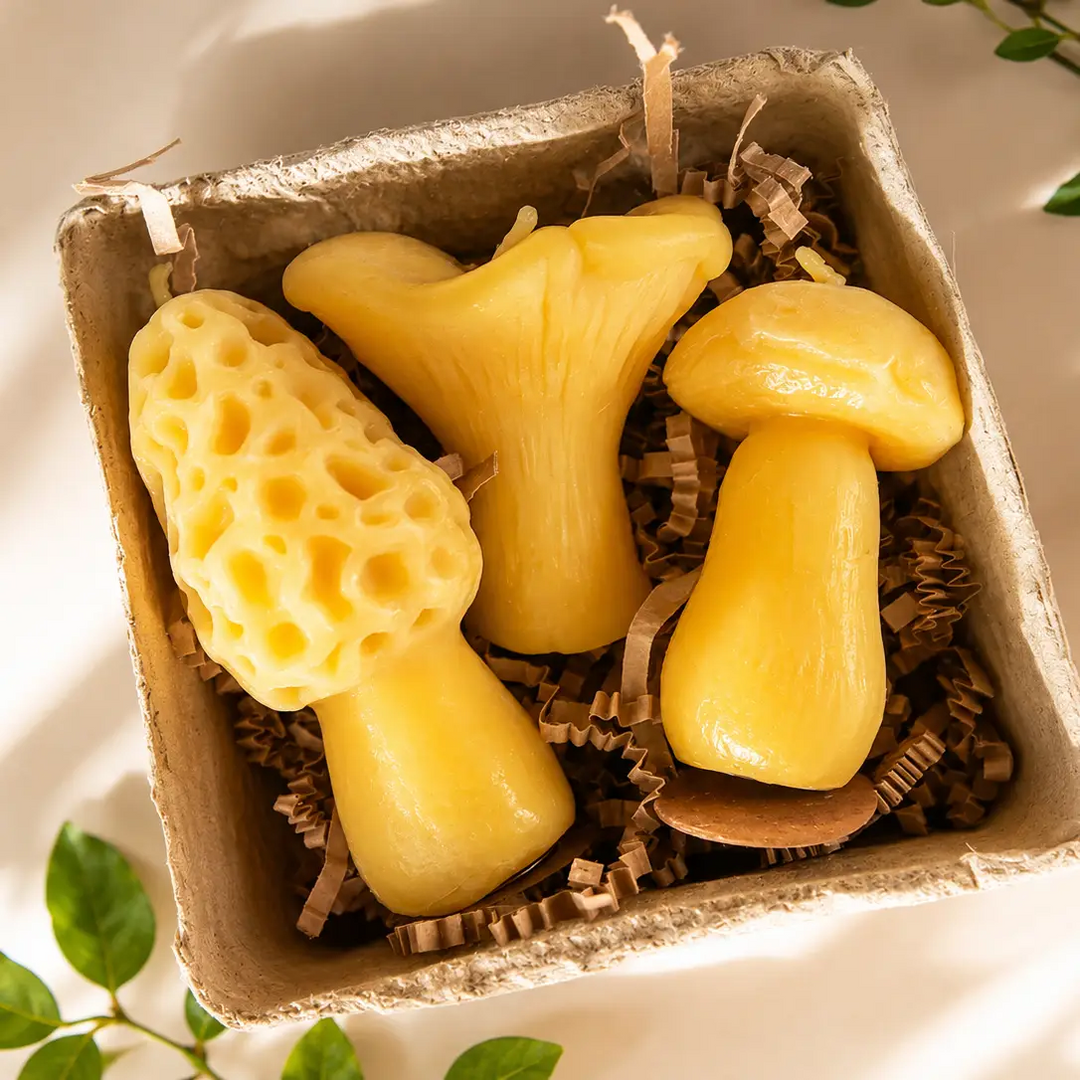 Three yellow mushroom-shaped items arranged in a small brown cardboard box filled with crinkle paper, photographed from above on a light surface with soft shadows and a few green leaves at the edges. Available at Luca Essentials in Los Angeles. 