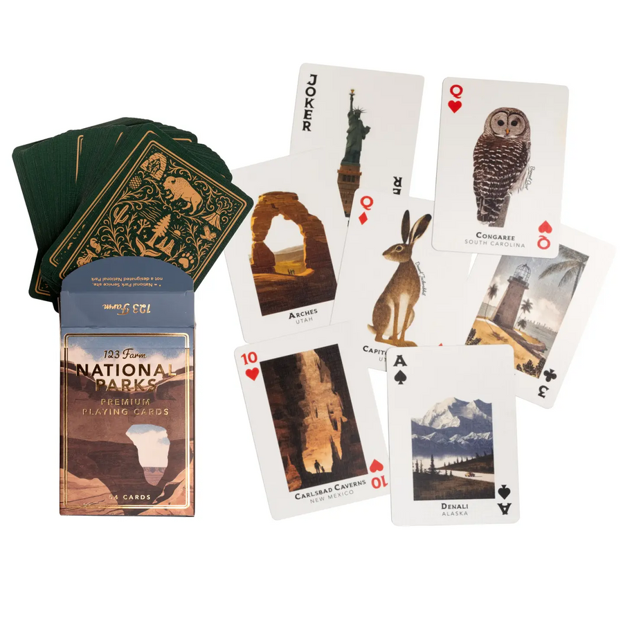National Parks playing cards set with a blue and brown illustrated box, a fanned deck of green-backed cards, and several sample cards showing national park illustrations on a white background. Available at Luca Essentials in Los Angeles. 