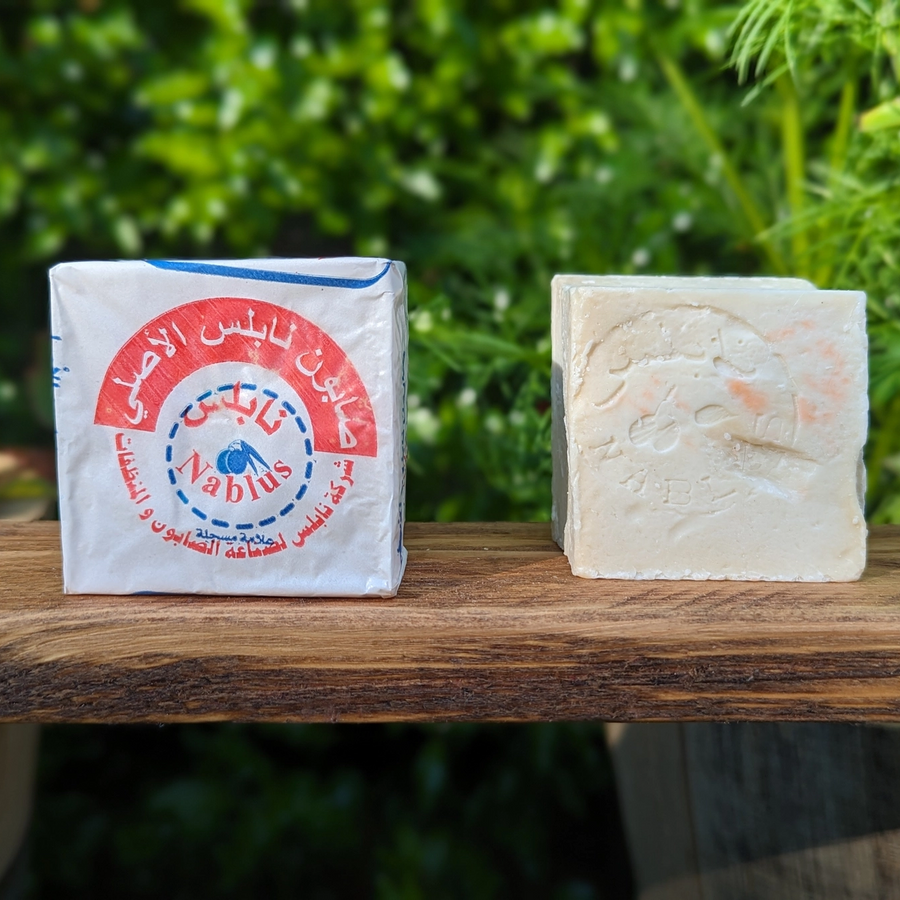 Nablus soap bar and packaging on a wooden surface with a green leafy background. Available at Luca Essentials in Los Angeles. 