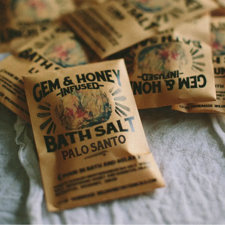 Bath salt packets labeled 'Gem & Honey Infused Bath Salt Palo Santo' on a textured surface. Available at Luca Essentials in Los Angeles. 