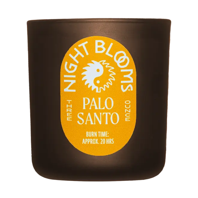 A dark brown candle jar with a prominent yellow oval label reading 'Night Blooms Palo Santo' on a white background. Available at Luca Essentials in Los Angeles. 