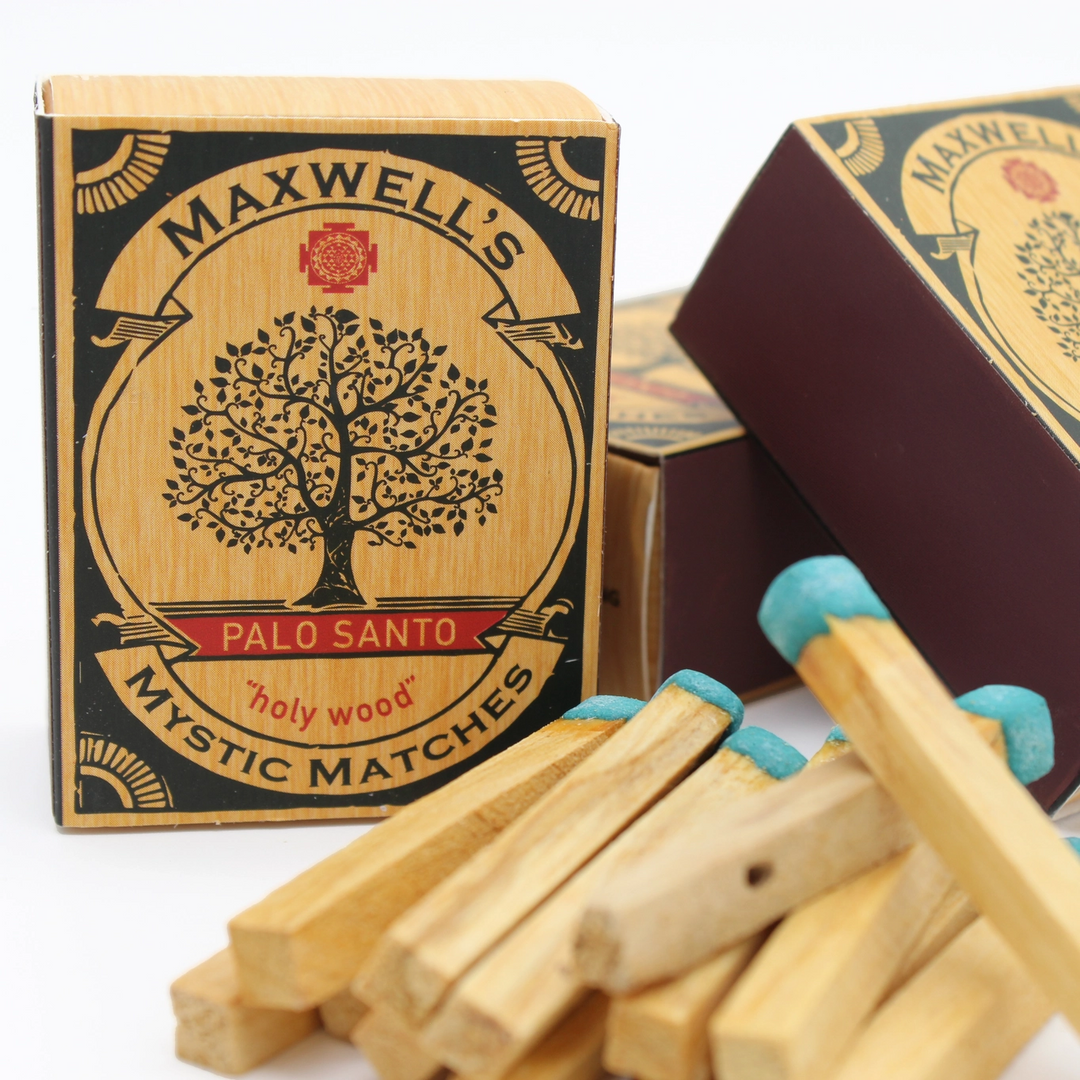 Maxwell's Palo Santo Mystic Matches with palo santo matchsticks with blue tips in a pile in front of multiple packages on a white background. Available at Luca Essentials in Los Angeles. 