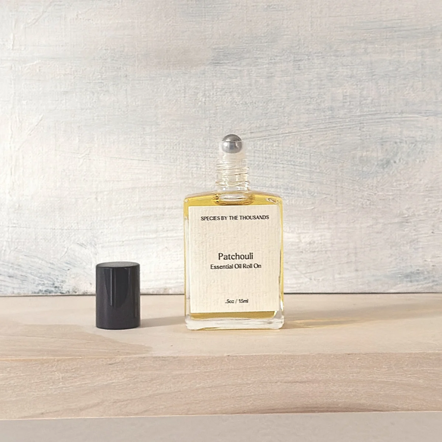 Patchouli essential oil roll-on bottle and a black cap on a wooden surface with a light background. Available at Luca Essentials in Los Angeles. 