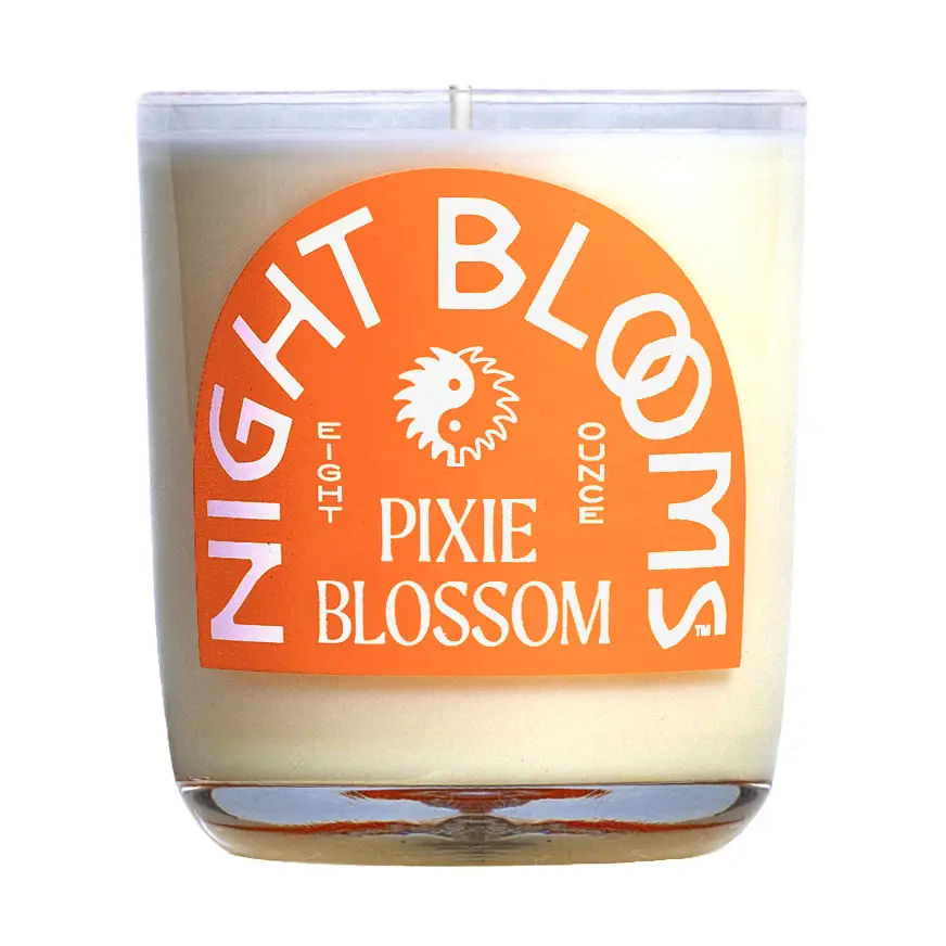 Candle with 'Night Blooms' and 'Pixie Blossom' orange label on a white background. Available at Luca Essentials in Los Angeles. 