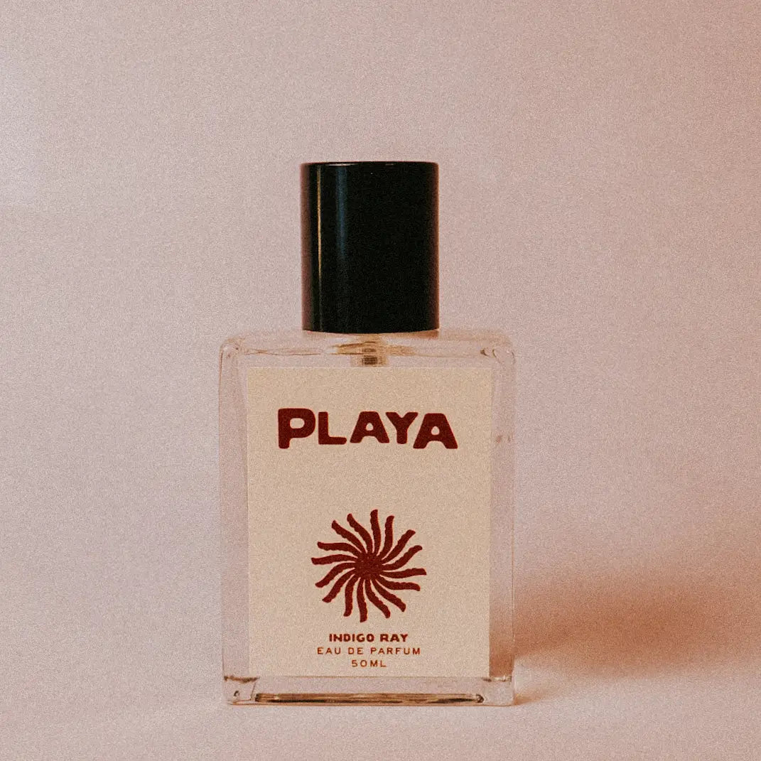 Playa perfume bottle with a beige label on a light pink background with black cap and red illustration on the label. Available at Luca Essentials in Los Angeles. 