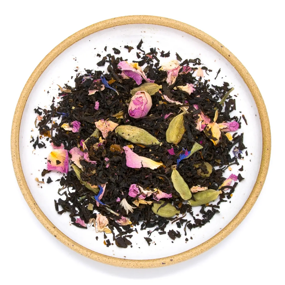 rose petals, cardamom spice and other herbal tea ingredients on a white plate with beige border on a white background. Available at Luca Essentials in Los Angeles. 