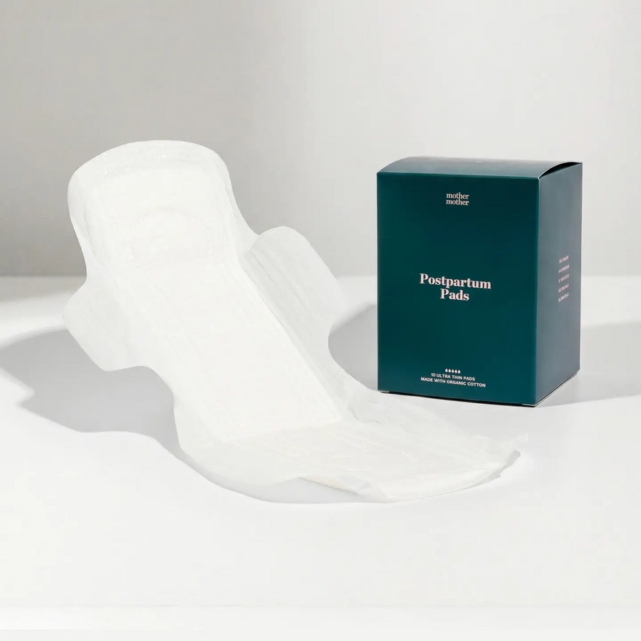 Box of postpartum pads with an opened white  pad with wings on a white surface with a neutral background. Available at Luca Essentials in Los Angeles. 