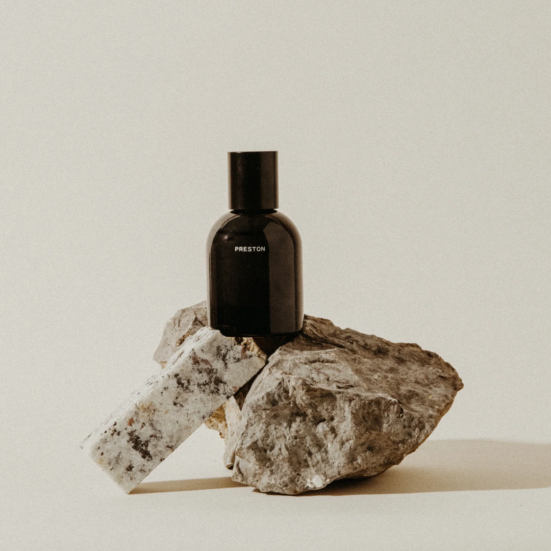 Black bottle labeled 'PRESTON' on a rock with a neutral background. Available at Luca Essentials in Los Angeles.