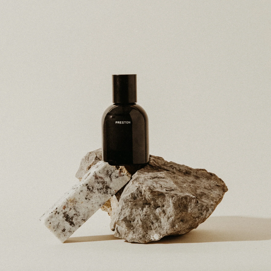 Black bottle labeled 'PRESTON' on a rock with a neutral background. Available at Luca Essentials in Los Angeles.