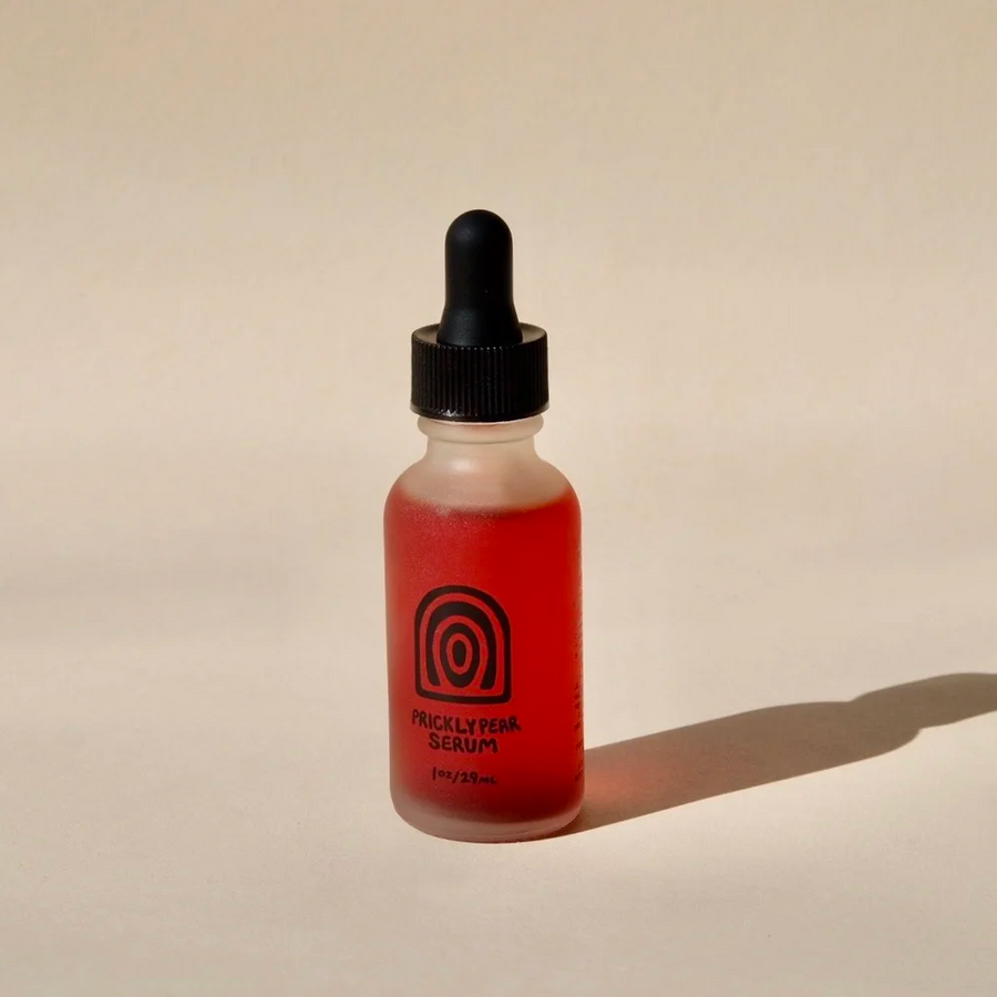 Bottle of red liquid with a black dropper  with the title "Prickly Pear Serum" and a black circular illustration, on a beige background. Available at Luca Essentials in Los Angeles. 