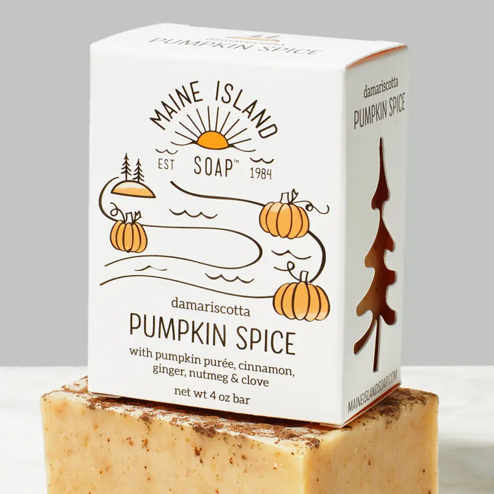Branded soap bar in box with the logo 'Maine Island Soap' and an illustration of pumpkins. The scent 'Pumpkin Spice' is located underneath the illustration. Box of bar soap is sitting on top of an orange and brown flecked bar soap without packaging. Available at Luca Essentials in Los Angeles. 