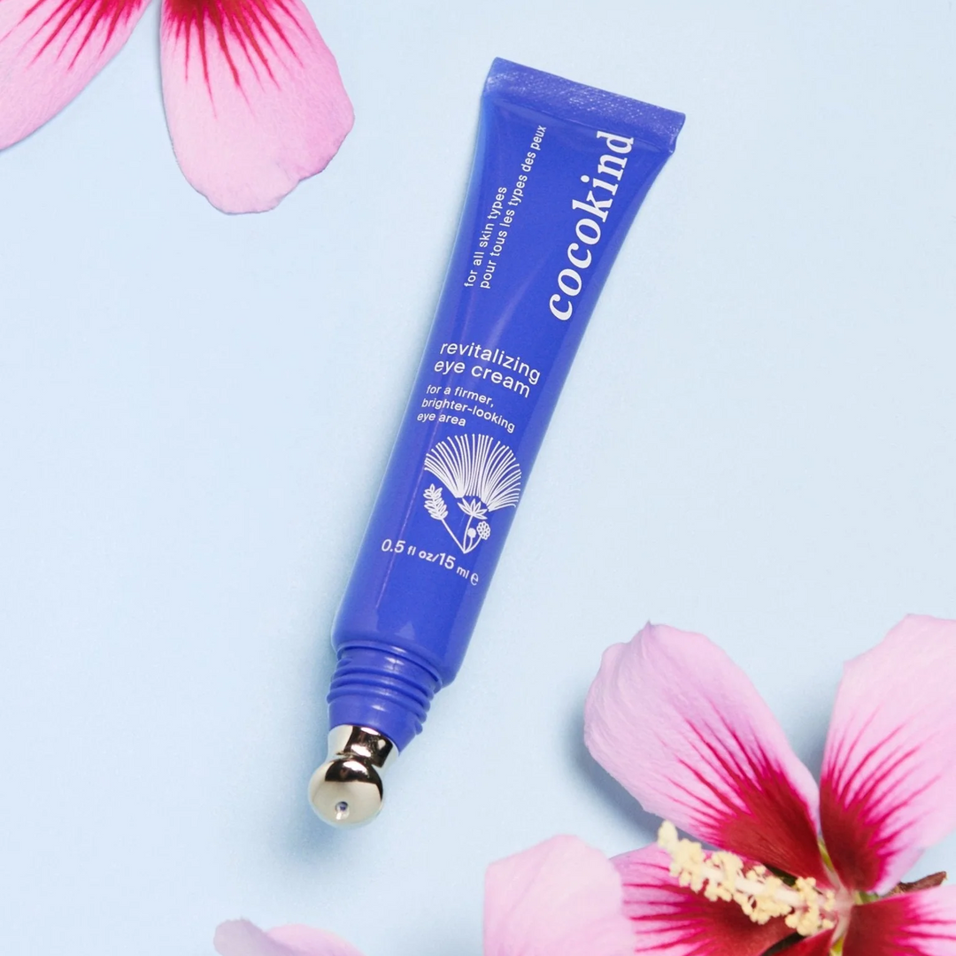 Blue Cocokind eye cream tube with pink hibiscus flowers in the corners on a light blue background. Available at Luca Essentials in Los Angeles. 