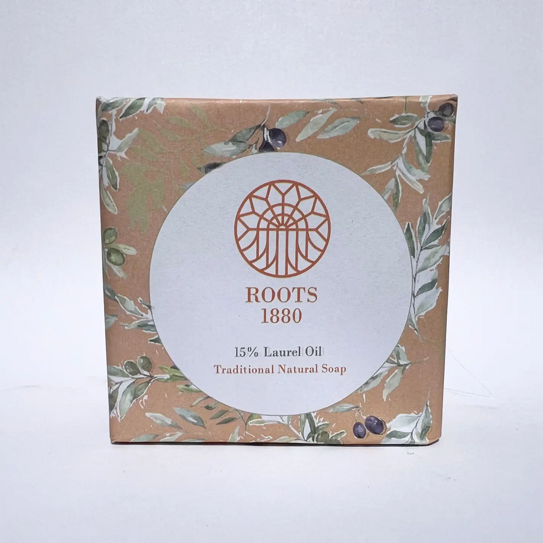 A square box of Roots 1880 Traditional Natural Soap with 15% Laurel Oil, featuring a brown kraft paper background with green and white botanical illustrations and a large white circular label in the center. Available at Luca Essentials in Los Angeles. 
