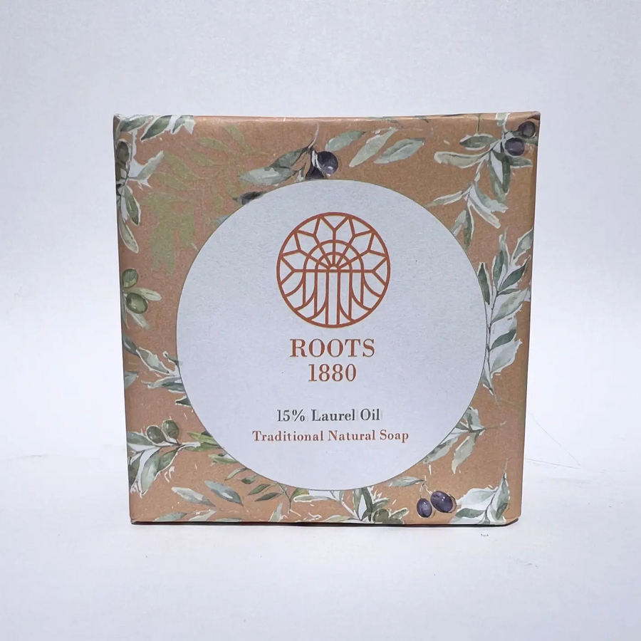 A square box of Roots 1880 Traditional Natural Soap with 15% Laurel Oil, featuring a brown kraft paper background with green and white botanical illustrations and a large white circular label in the center. Available at Luca Essentials in Los Angeles. 
