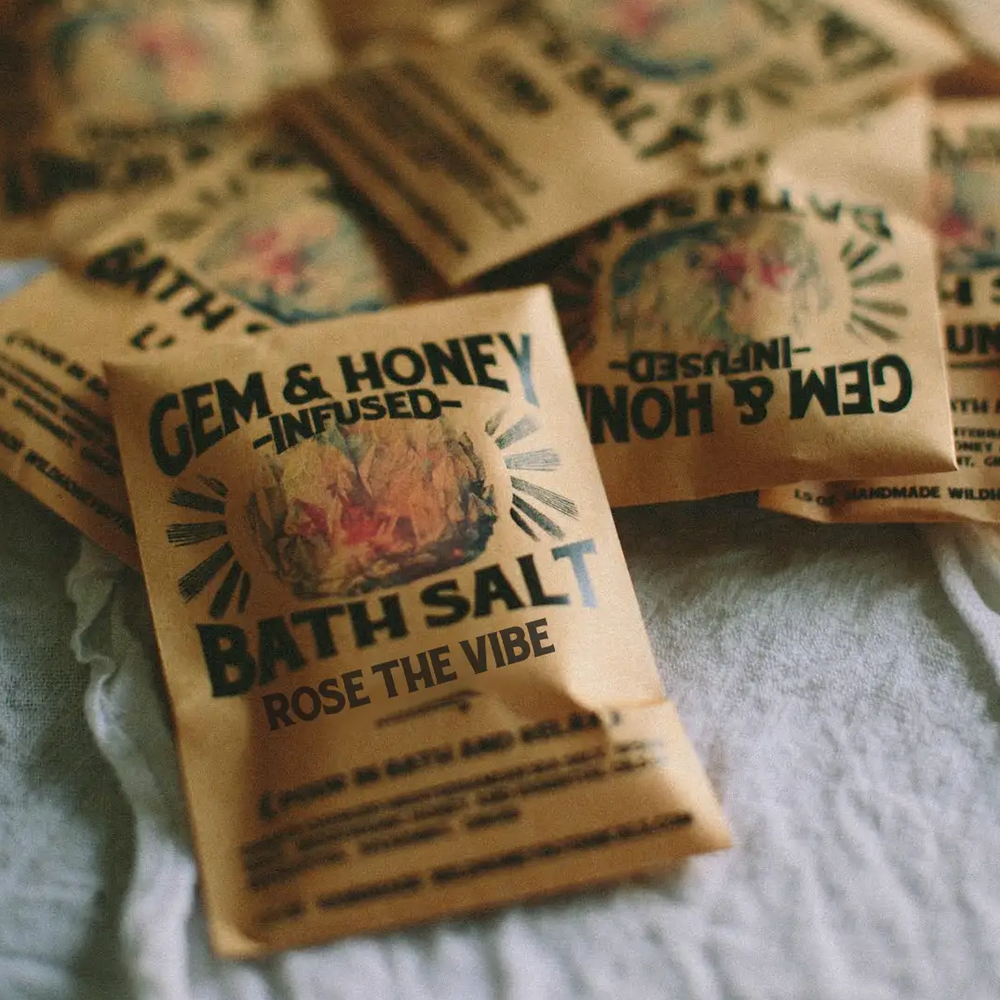Bath salt packets with 'Gem & Honey' branding and the text 'ROSE THE VIBE' on a textured surface. Available at Luca Essentials in Los Angeles. 