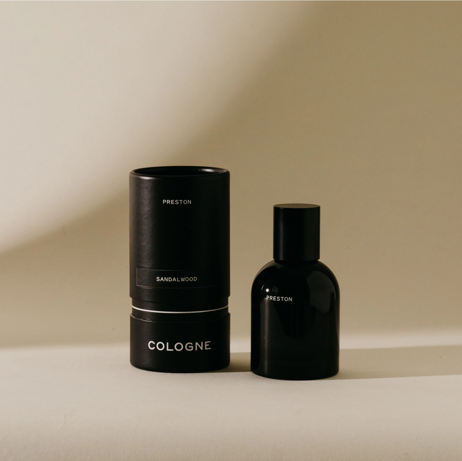 Black cologne bottle and cylindrical container on a beige background. Available at Luca Essentials in Los Angeles. 