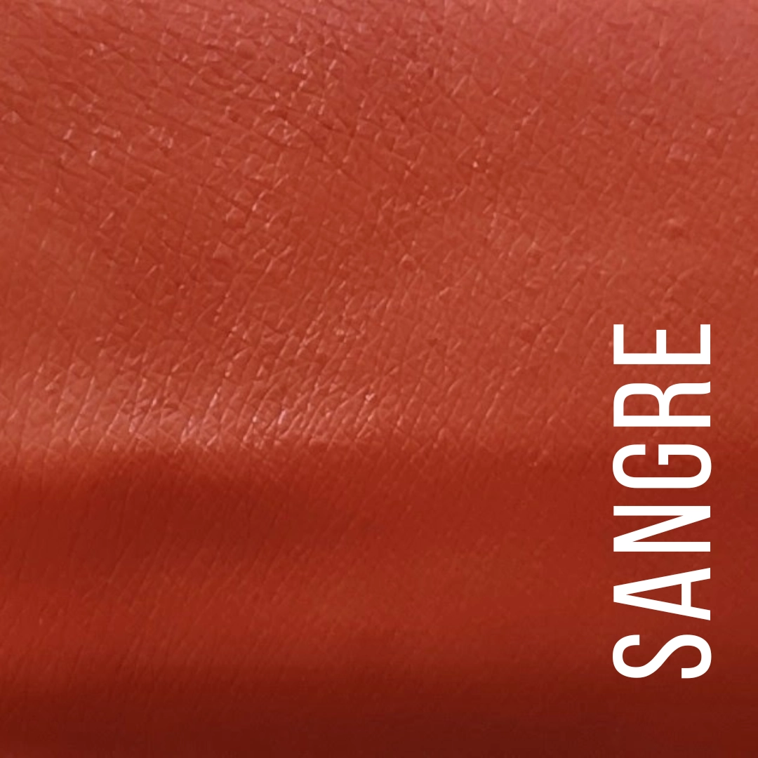 A close-up color swatch of textured leather in a deep red-orange shade, labeled with the word 'SANGRE' in white vertical text on the right side. Available at Luca Essentials in Los Angeles. 
