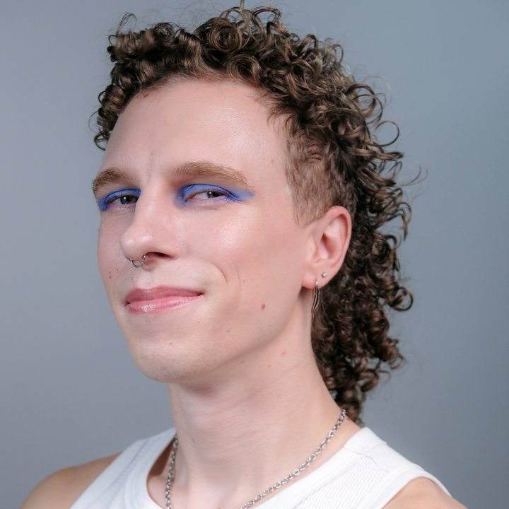 Selenite - Pale toned person with curly hair and blue eye makeup against a gray background.
Available at Luca Essentials in Los Angeles. 
