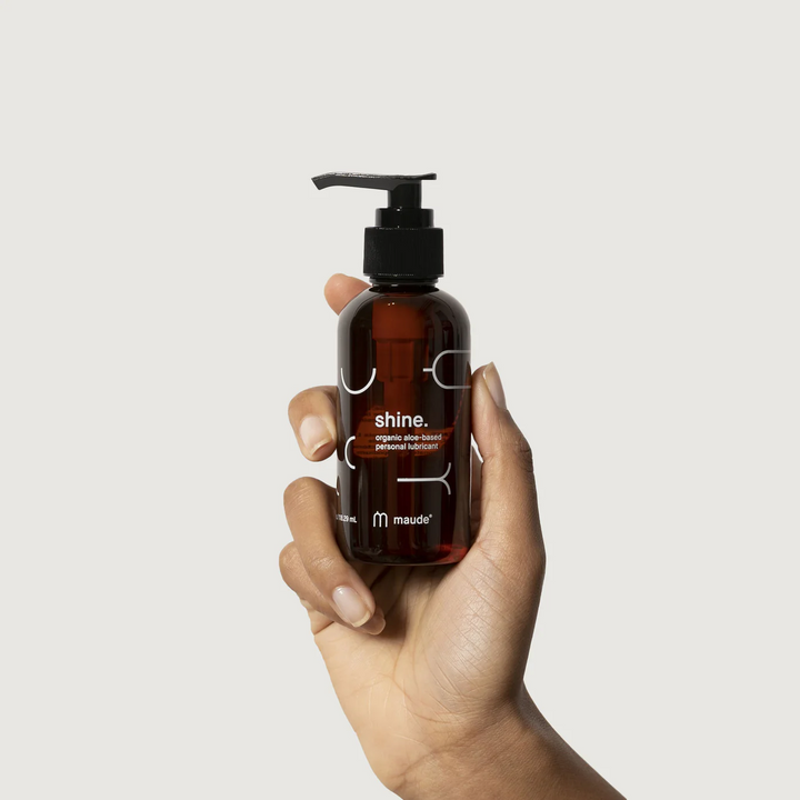 Hand holding a 4oz amber colored bottle of shine aloe based lubricant on a white background. 

Formulated with organic aloe and purified water, shine delivers long-lasting glide while supporting the body’s natural moisture. 

Available at Luca Essentials in Los Angeles. 