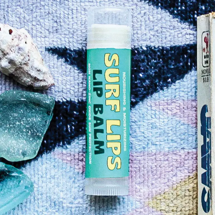Surf Lips lip balm on a textured surface with rocks and a book. Available at Luca Essentials in Los Angeles. 
