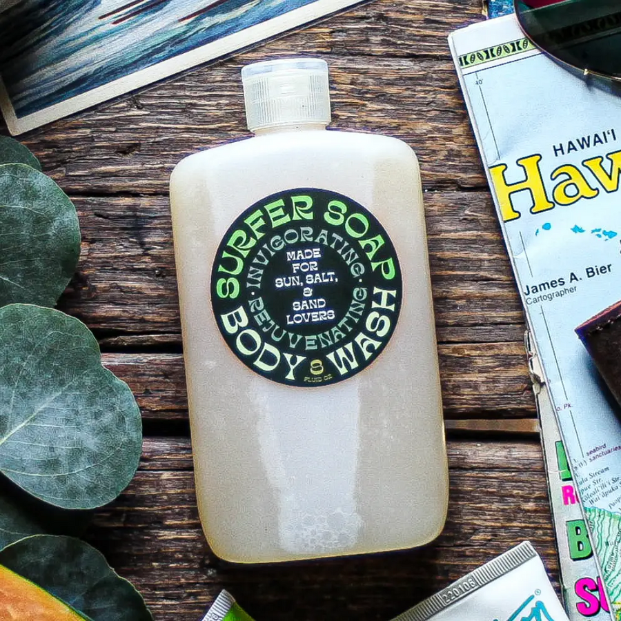 Surfer Soap bottle on a wooden surface with a magazine and plant leaves. Available at Luca Essentials in Los Angeles. 