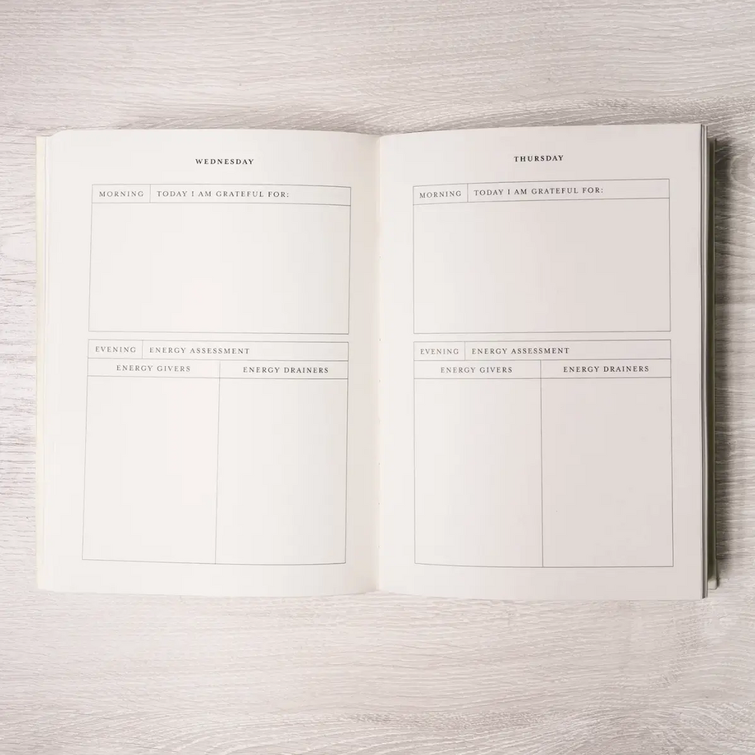 Open planner with daily gratitude and energy assessment pages on a light wooden surface. Available at Luca Essentials in Los Angeles. 