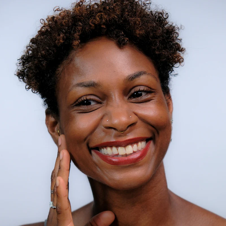 Tiger's Eye - Woman with medium to dark skin tone and  a bright smile and a white background. Available at Luca Essentials in Los Angeles. 