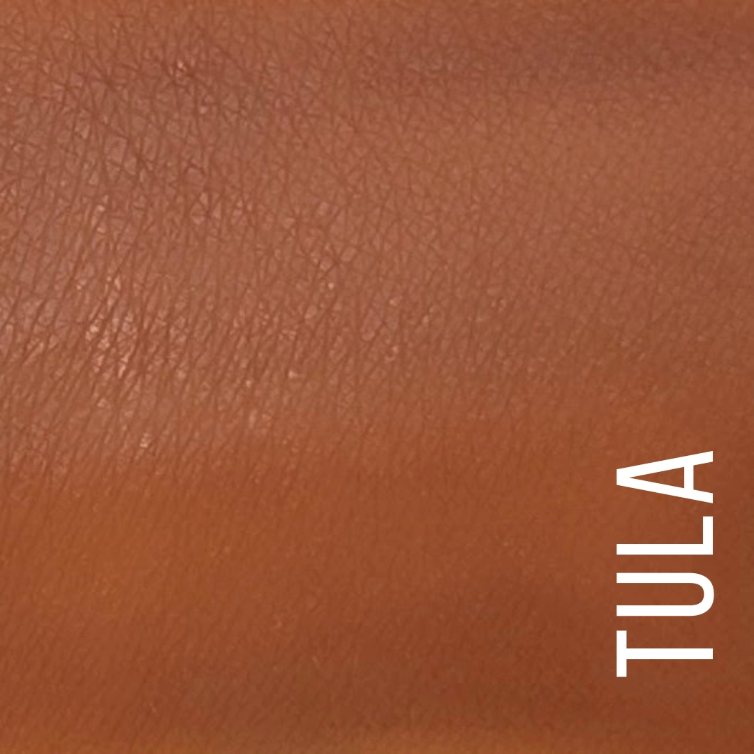 A close-up color swatch of a warm medium brown leather-like texture with the word 'TULA' printed vertically in white in the lower right corner. Available at Luca Essentials in Los Angeles.