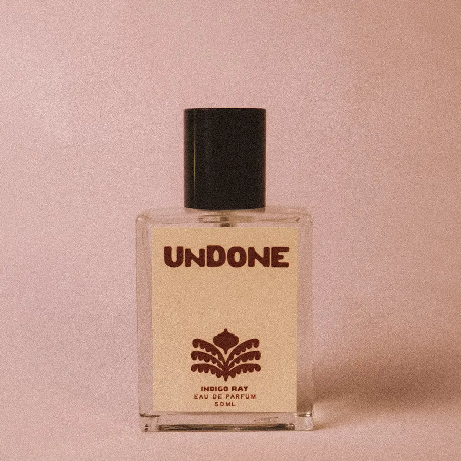 Glass perfume bottle labeled 'UNDONE' on a pink background with a black cap and a red illustration on the label. Available at Luca Essentials in Los Angeles. 