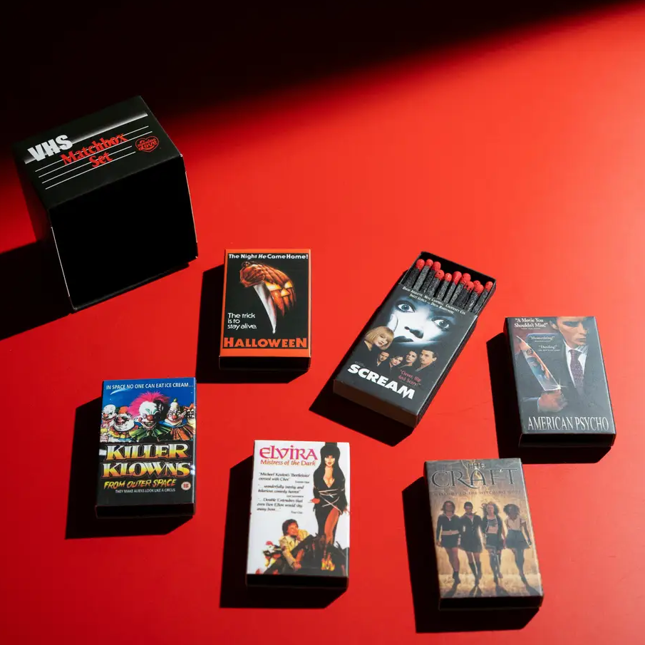Six horror-themed card decks and one black box arranged on a red studio surface with dramatic shadows. Visible deck titles include Scream, American Psycho, The Craft, Elvira, Halloween, and Killer Klowns. Available at Luca Essentials in Los Angeles. 