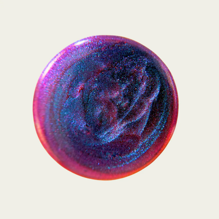 Multicolored glittery purple, pink, blue nail polish on a light gray background. Available at Luca Essentials in Los Angeles. 