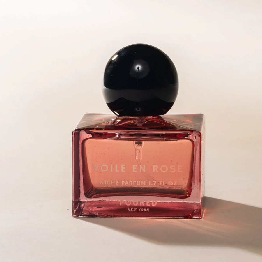 Dark pink glass perfume bottle with black cap and the name "voile en rose' on the bottle on a light background. Available at Luca Essentials in Los Angeles. 
